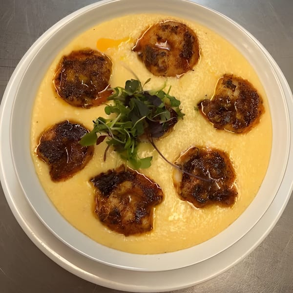 Seared scallops in a creamy yellow sauce, garnished with microgreens, served on a white plate.