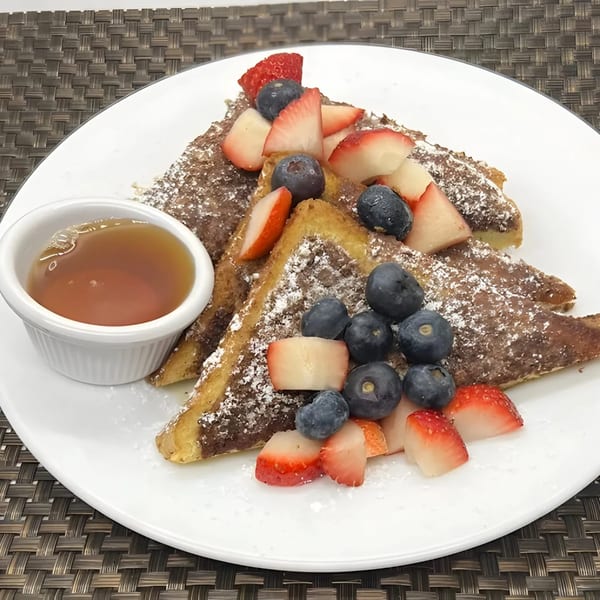 French toast triangles with powdered sugar, blueberries, strawberries, and a side of syrup on a white plate.