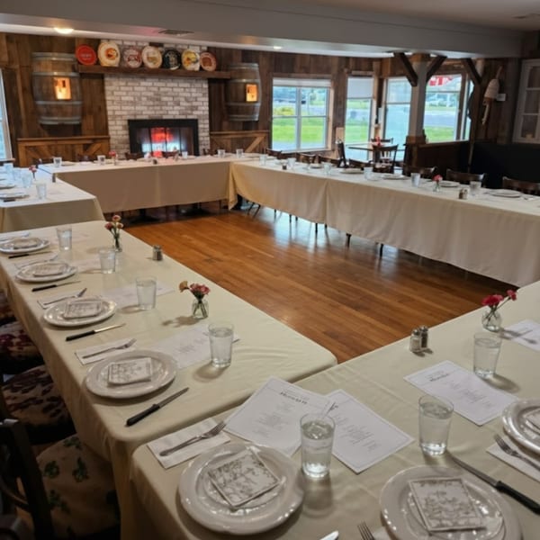 A dining room at The Clam Bar with U-shaped tables set for a meal, featuring a fireplace and rustic decor.