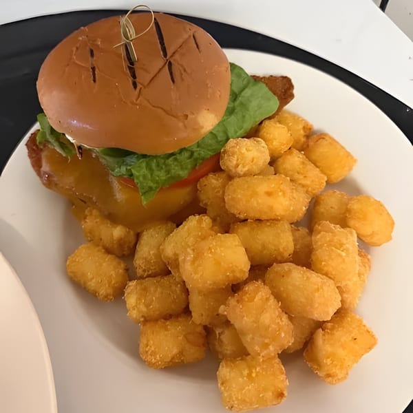 A Clam Bar seafood sandwich with melted cheese, lettuce, and tomato, served with tater tots.