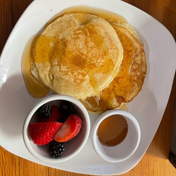 Golden pancakes drizzled with syrup, served with fresh strawberries and blackberries on a white plate.
