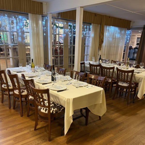 Dining room at The Clam Bar with set tables, wooden chairs, and string lights on windows.