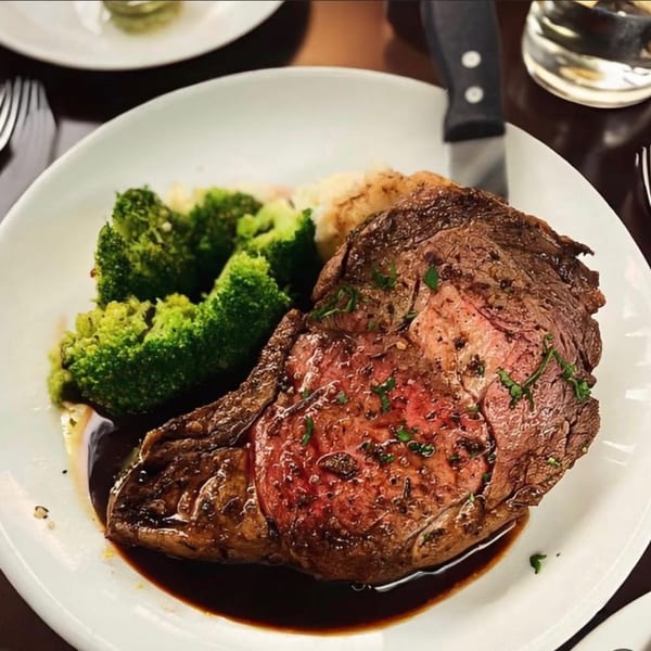A prime rib steak with gravy, mashed potatoes, and broccoli on a white plate.