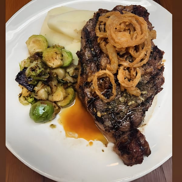 Grilled steak topped with crispy onion rings, mashed potatoes, and roasted Brussels sprouts on a white plate.