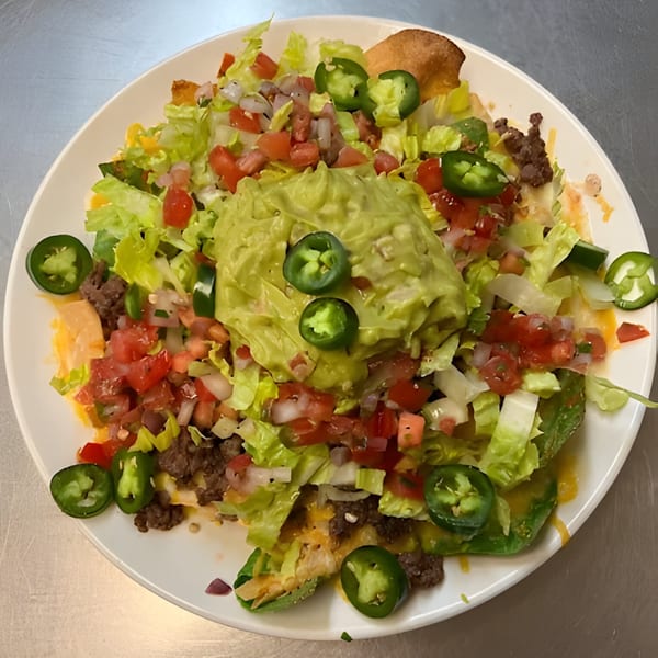 A plate of nachos with ground beef, lettuce, tomatoes, jalapeños, and a large dollop of guacamole.